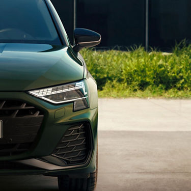 Close-up of a green car's front end with sleek headlights and a modern design.