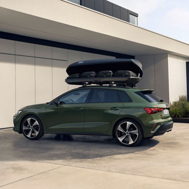 Green Audi car with roof box parked beside a building.