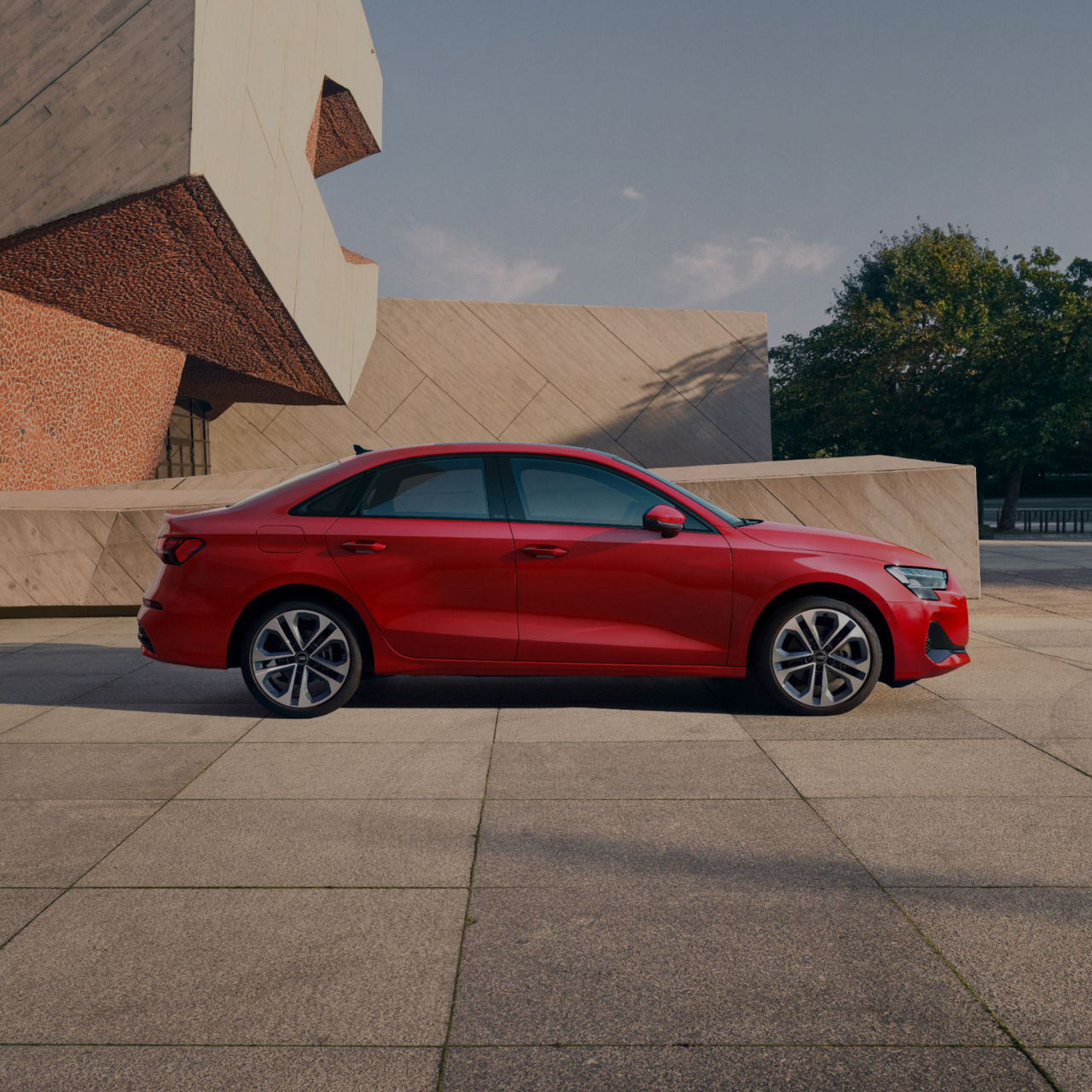 Red sedan parked near a modern building with geometric shapes.