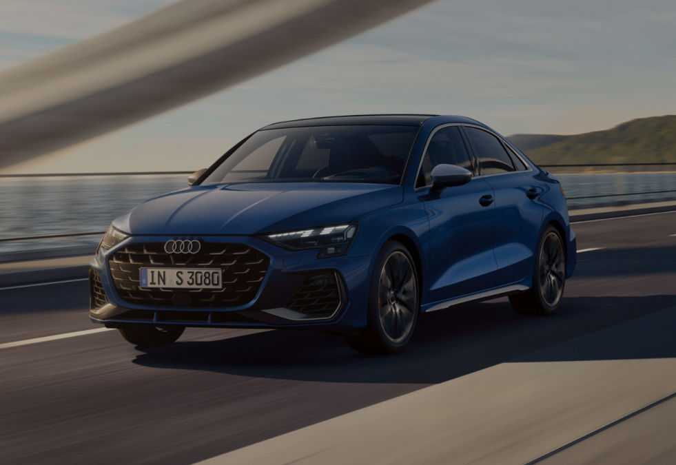 A blue Audi S3 Saloon car driving on a road with a coastal backdrop during dusk.