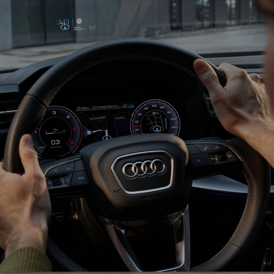 Driver's hands on an Audi steering wheel with a view of the dashboard.