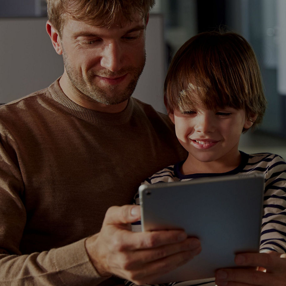 A man with a kid holding a tablet together, with one in a brown sweater and the other in a striped top.