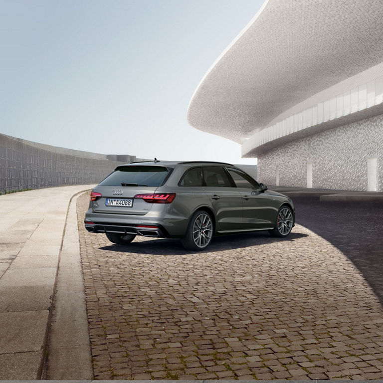 A grey car parked beside a distinctive white textured wall on a sunny day.