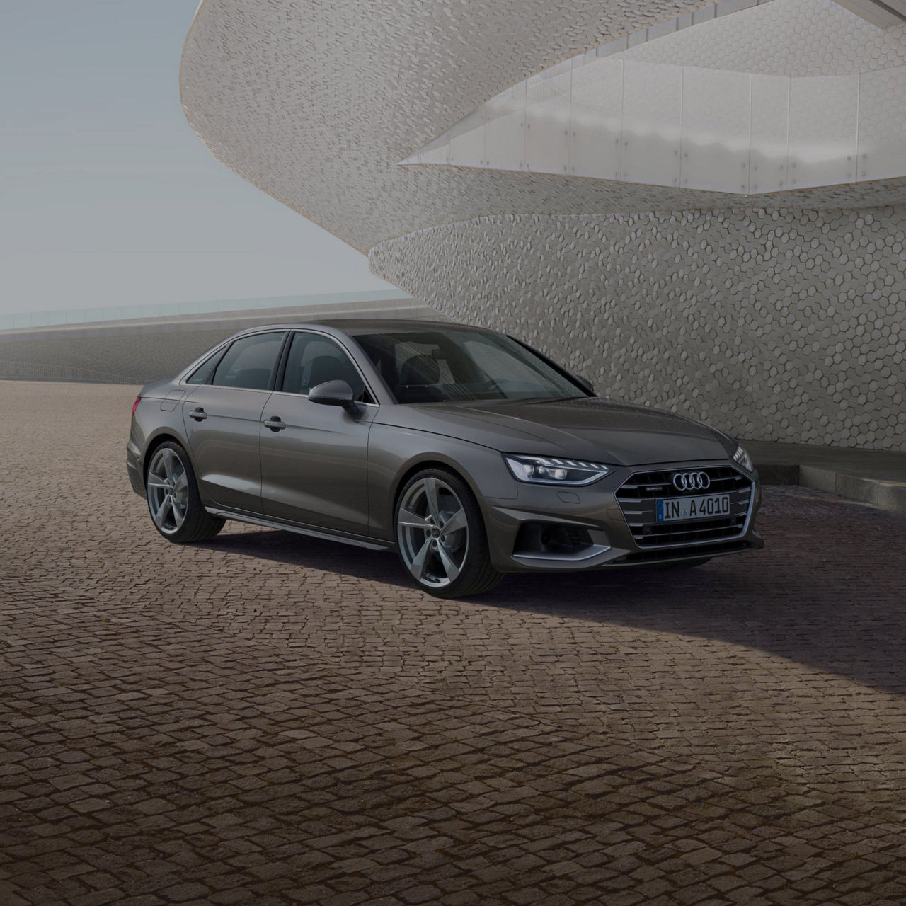 A grey Audi sedan parked in front of a textured building facade under a clear sky.