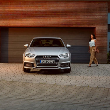 A silver Audi parked in front of a garage with a person walking by.