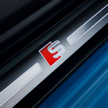 A close-up of a metallic car detail with a red and silver 'S' emblem.