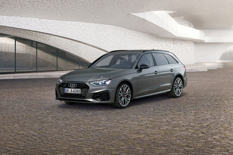 A grey car parked in front of a futuristic building with a textured facade.