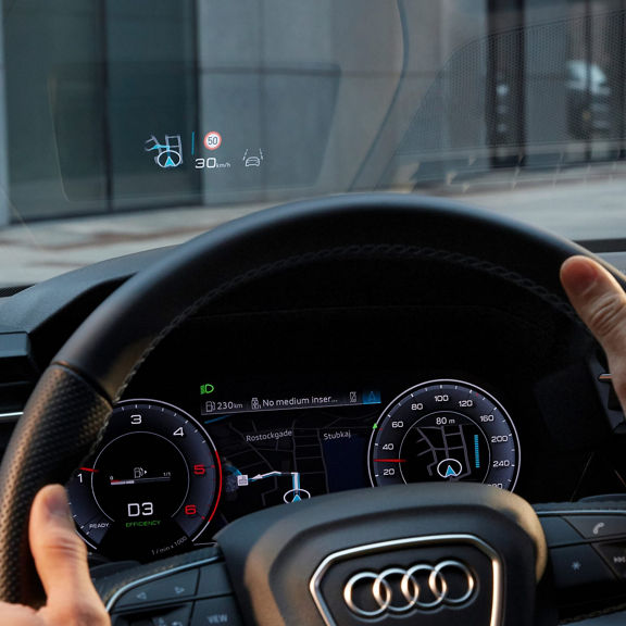 Driver's view of a car's steering wheel and digital dashboard displaying speed and navigation.