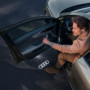 A person getting into an Audi with the logo projected onto the ground.