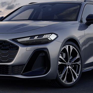 Close-up of a silver car's front end with sleek LED headlights and a distinctive grille at dusk.