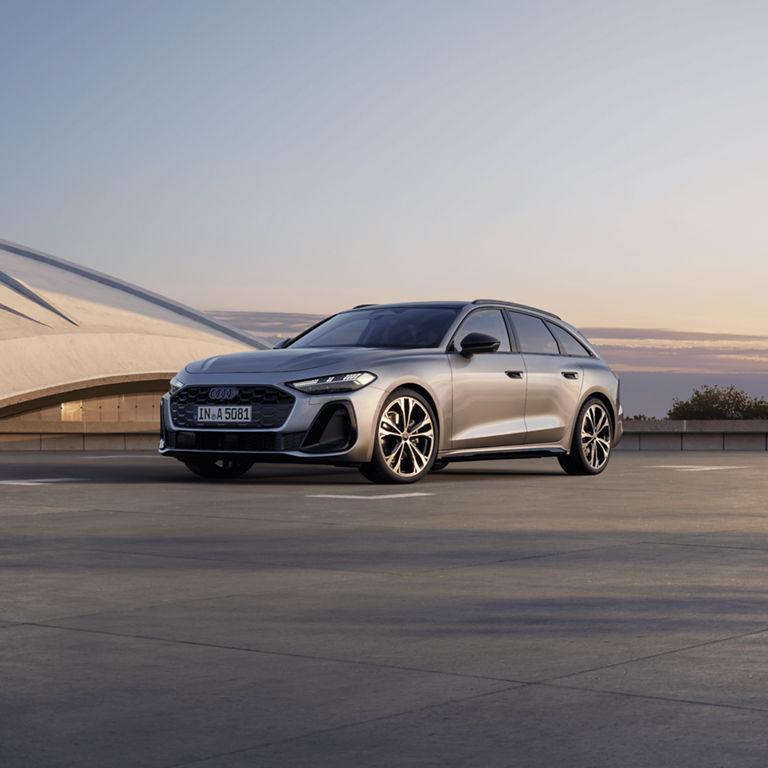 Silver Audi car parked at sunset with modern architecture in the background.