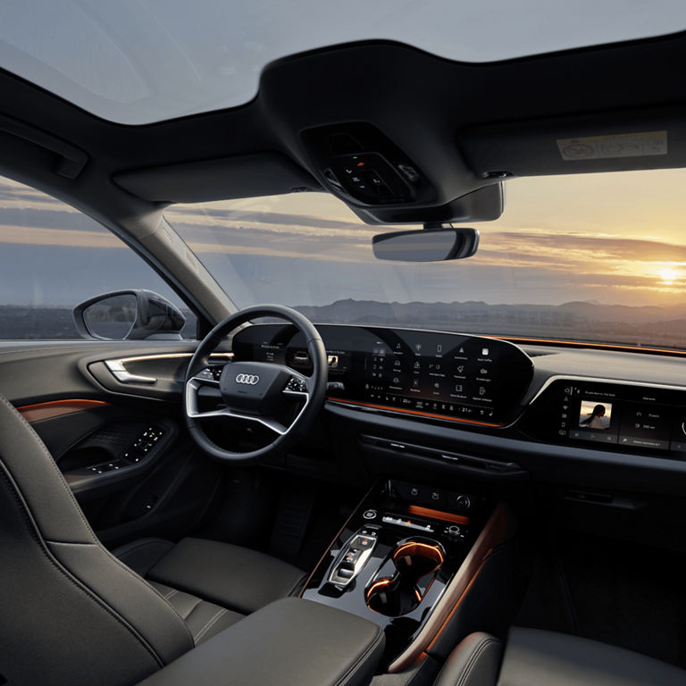 Interior view of a car with a dashboard display, steering wheel, and sunset outside the windshield.