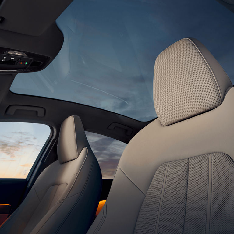 Interior view of a car showing a sunroof, headrest, and control buttons with a dawn sky outside.