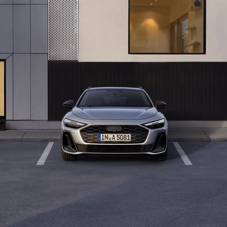 Silver Audi car parked in front of a modern building at twilight.