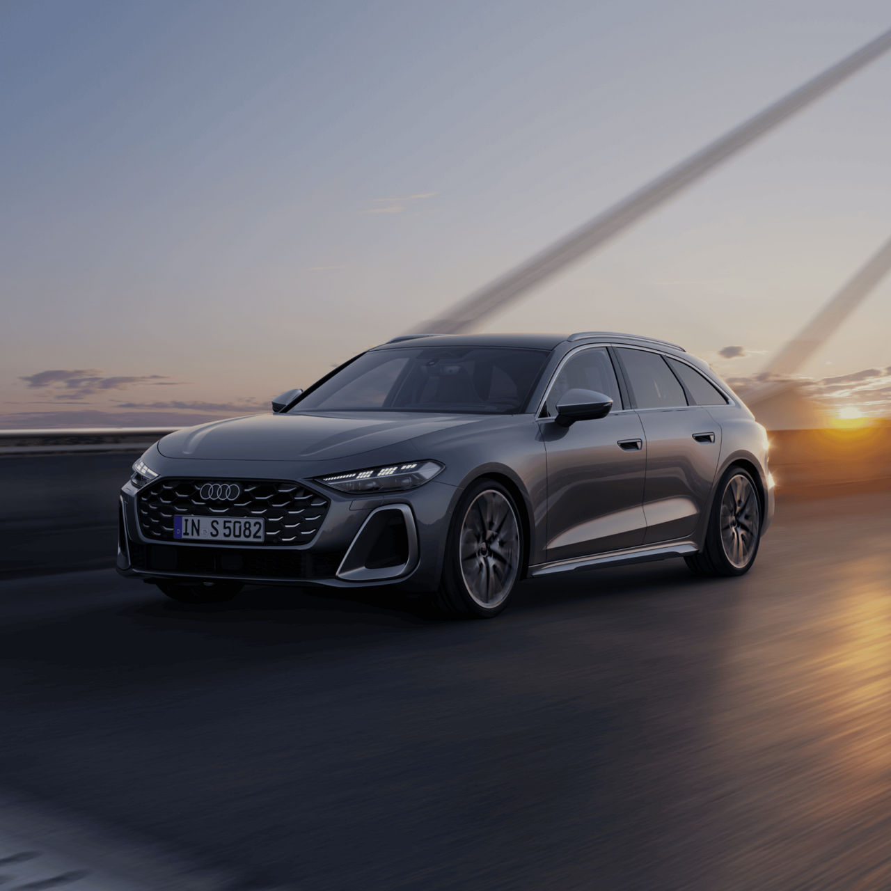 A grey Audi car driving on an open road at sunset.