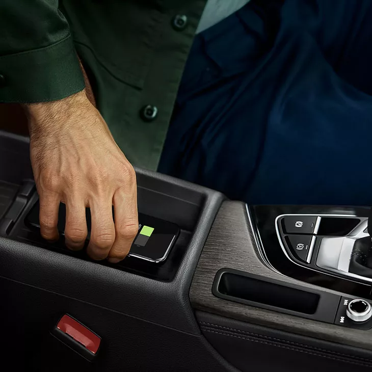 Person placing a smartphone on a car's wireless charging pad.