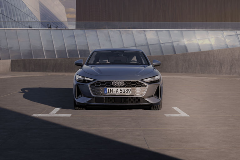 A Silver Audi parked in an outdoor lot with modern buildings in the background.