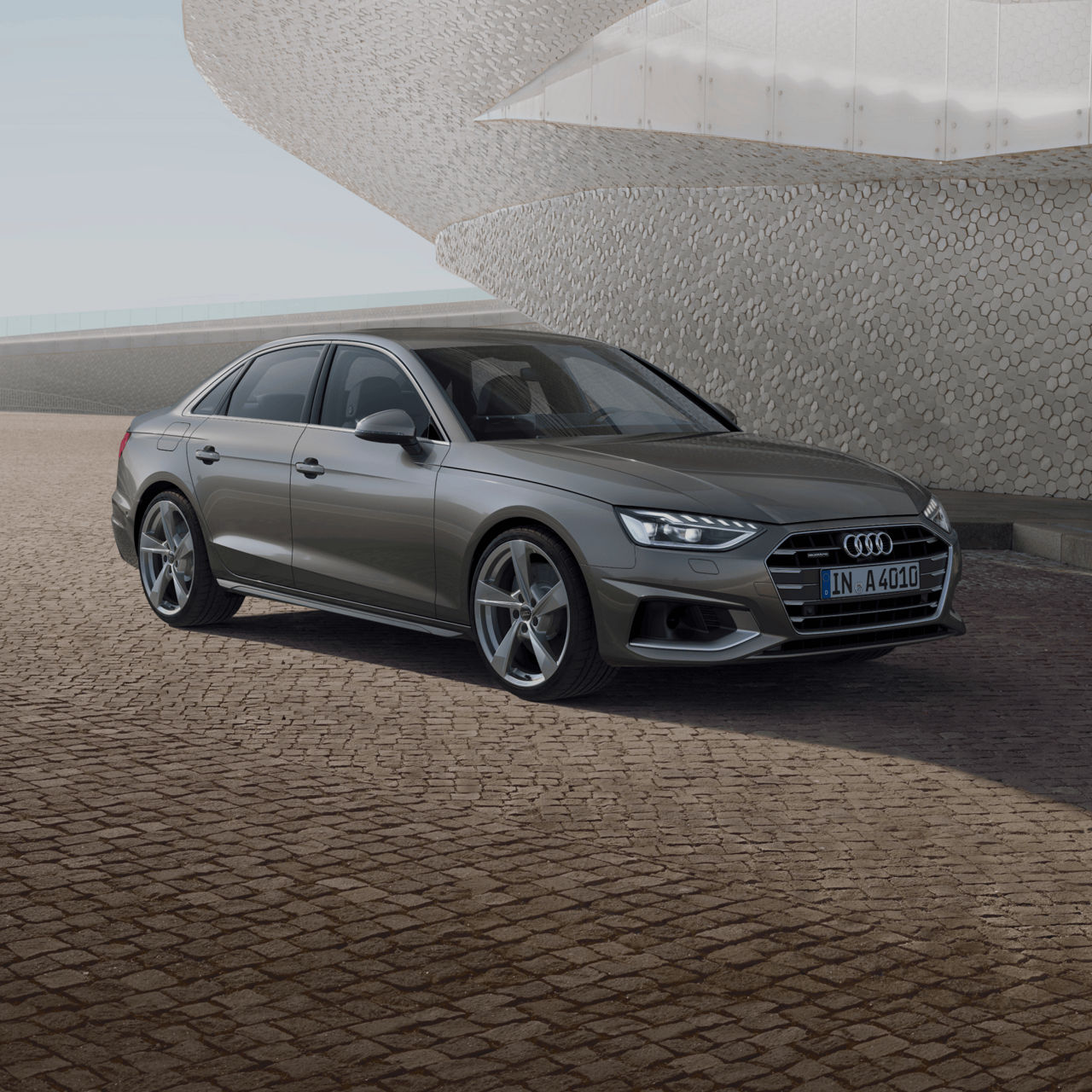 A grey Audi A4 Saloon parked in front of a modern building with a textured facade.