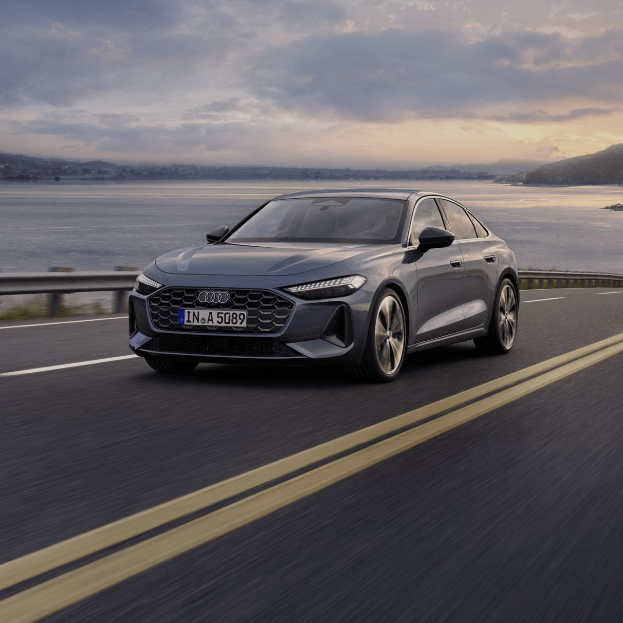 A grey Audi sedan driving on a coastal road at dusk.