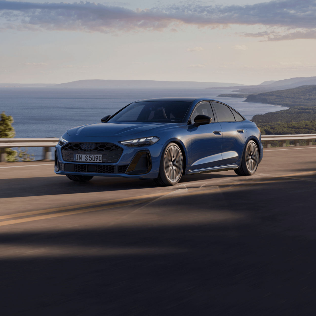 Blue Audi sedan driving along a coastal road with clear skies.