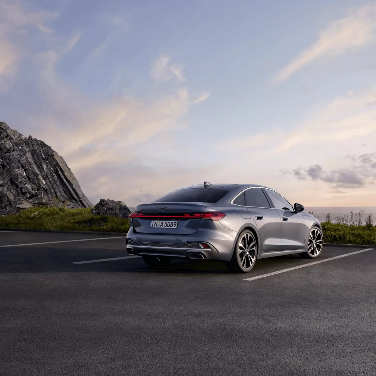 Silver sedan parked on coastal road at dusk with rocky cliff and sky in background.