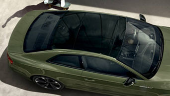 Top view of a green coupe with a person standing beside it holding a skateboard.