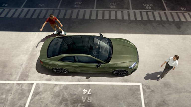 Aerial view of a green car in a parking lot with two individuals, one on a skateboard.