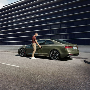 A person standing next to a green sedan in front of a modern building.