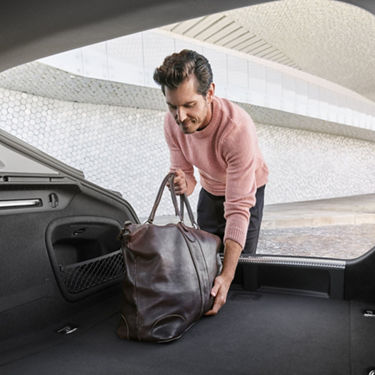 Person placing a leather duffel bag into a car trunk.