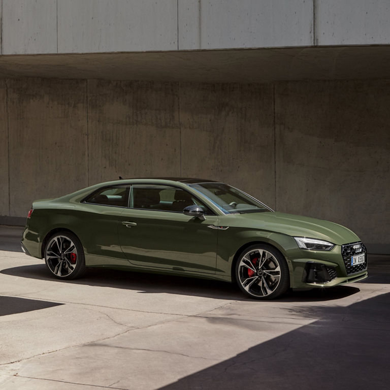 Green coupe car parked under a concrete overpass during daylight.