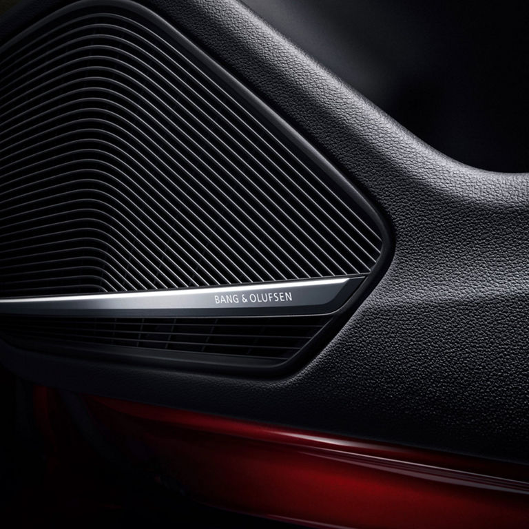 Close-up of a Bang & Olufsen car speaker grille with a metallic logo.