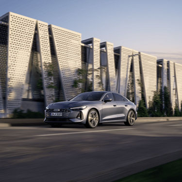 Silver sedan driving on road with unique patterned buildings in background.