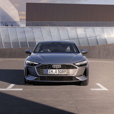 A silver Audi A5 Saloon car parked in front of a modern building under a clear sky.