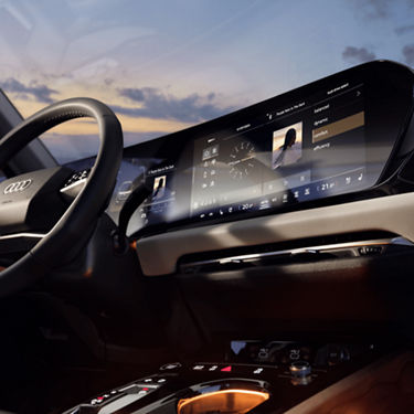 Interior view of a car with a focus on the steering wheel and a curved digital dashboard displaying settings at dusk.