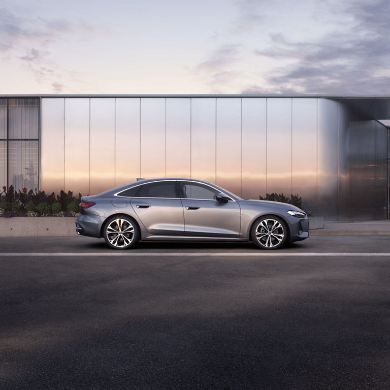 A sleek silver sedan parked beside a modern glass building at dusk.