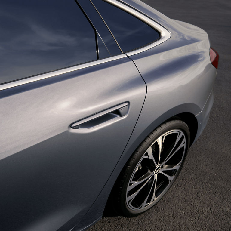 Close-up of a silver car's rear side panel and wheel.