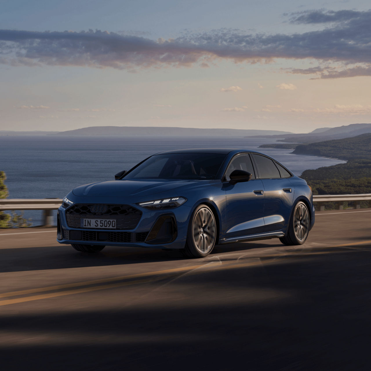 Blue Audi sedan driving along a coastal road at sunset.