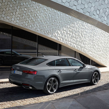 A grey Audi sedan parked by a building with a unique hexagonal-patterned facade.
