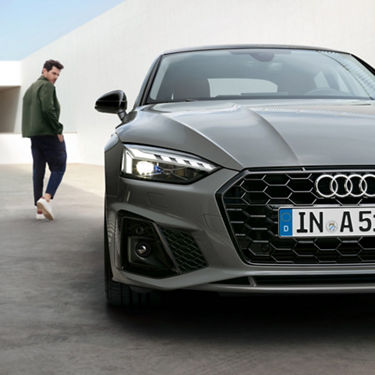 Close-up of a grey Audi car's front with a European license plate, parked in a minimalistic setting.