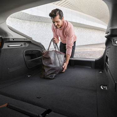 Person placing a leather bag in the trunk of a car.