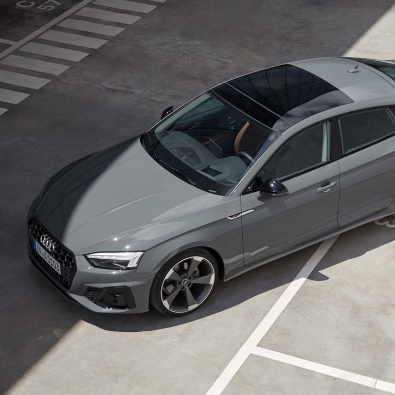 Aerial view of a grey Audi parked diagonally across the lines in a parking lot.