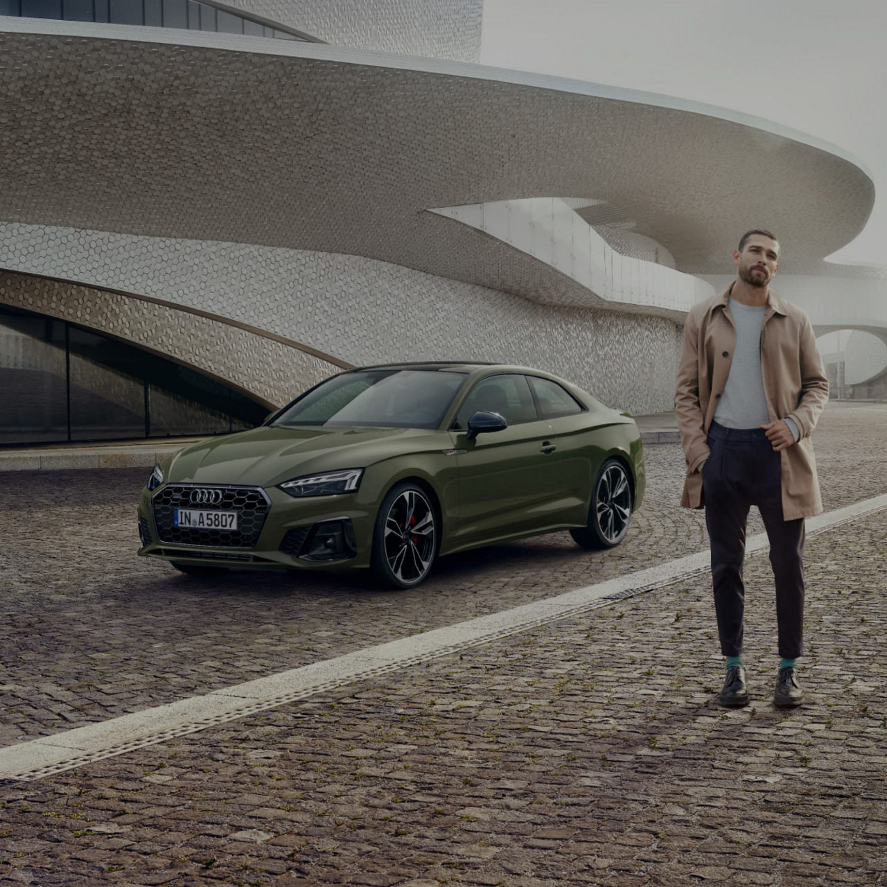 A green Audi car parked in front of a modern building with a person standing beside it.