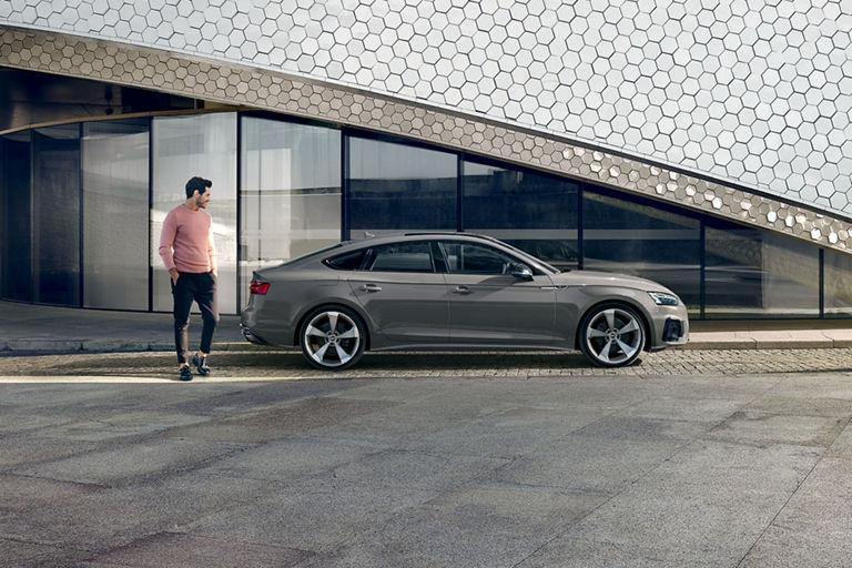 A grey Audi A5 Sportback parked outside a modern building with hexagonal patterns.