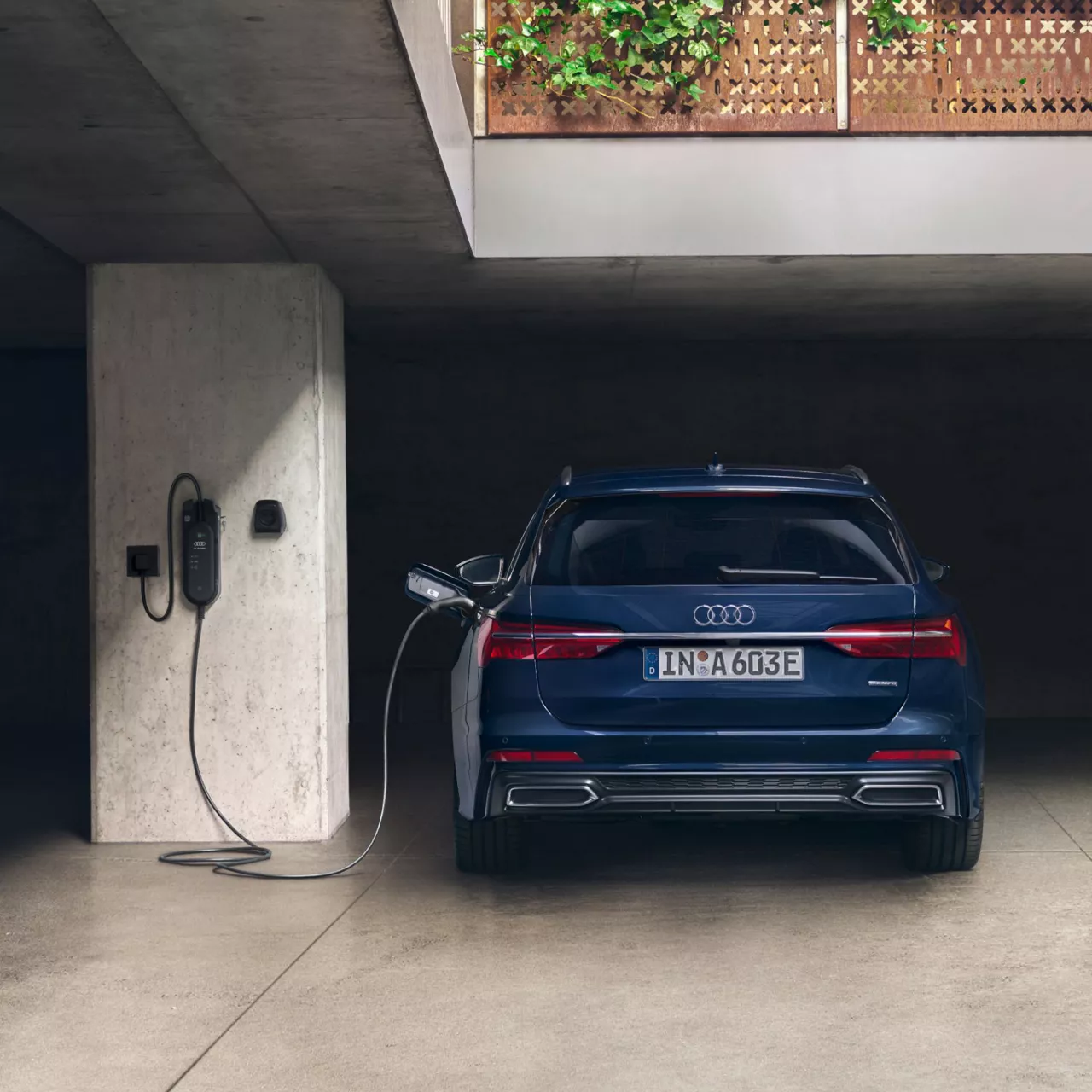 A blue Audi electric car charging at a wall-mounted station in a concrete garage.