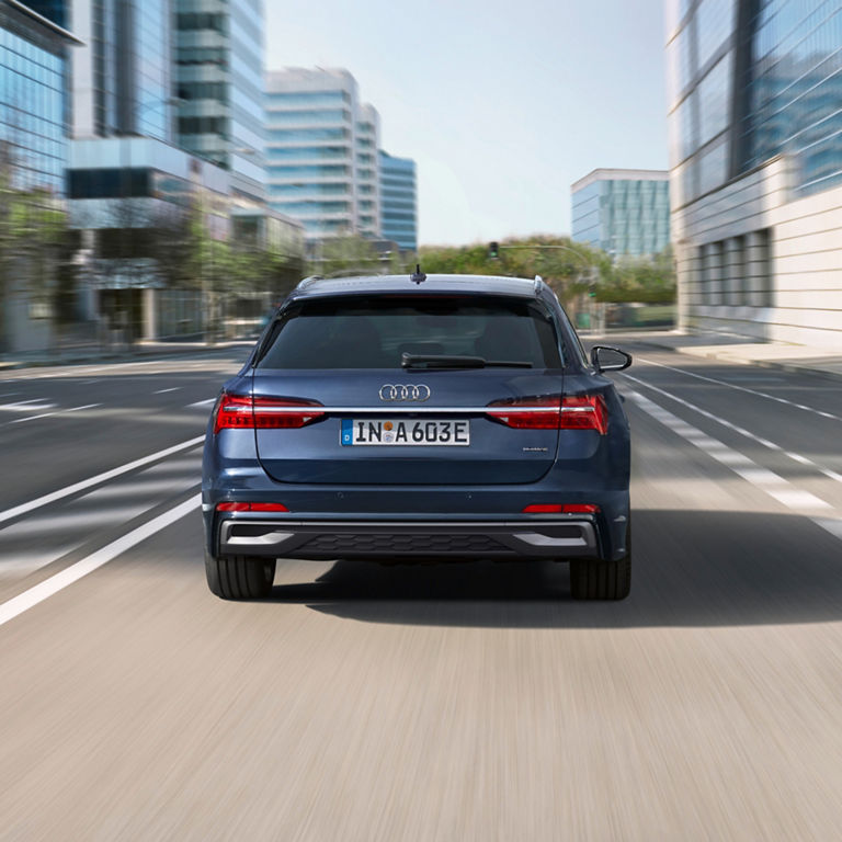 A blue Audi car driving on a city road, viewed from the rear.