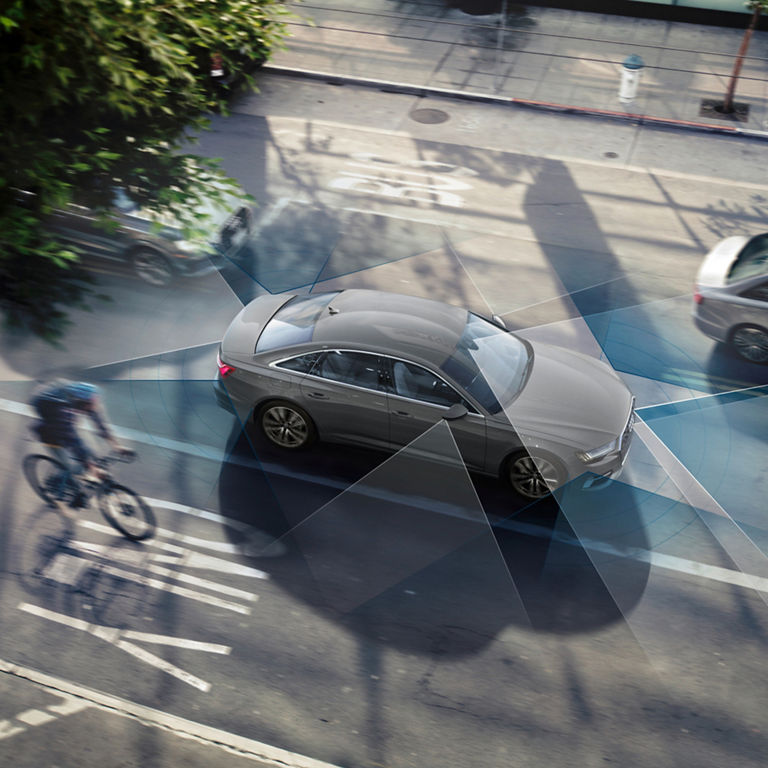 Aerial view of a sedan with sensor graphics overlay sharing the road with a cyclist.