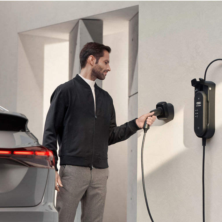 A person holding a charging plug near an electric vehicle wall charger.