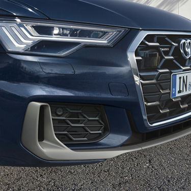 Close-up of a blue car's front left headlight, grille with emblem, and part of the bumper.