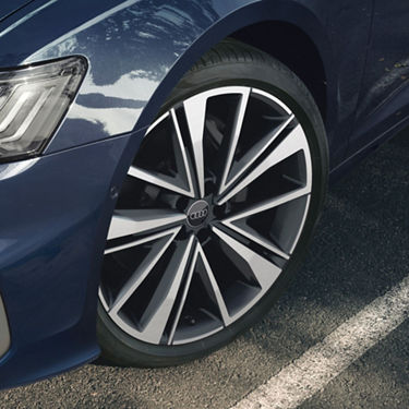 Close-up of a car's alloy wheel with a logo, parked on asphalt.