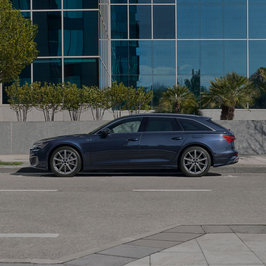 A blue sedan parked on a city street with a reflective glass building and palm trees in the background.